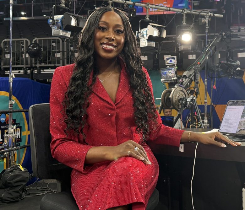 Chiney Ogwumike sits at a desk with a computer set up and a hat sitting on the desk as a camera light shines.