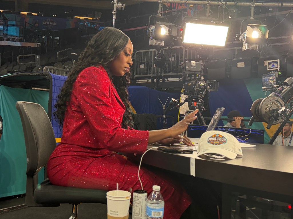 Wearing a red sequin suit, Chiney Ogwumike plays on her ipad as she prepares for the championship game. A white hat sits on the table.
