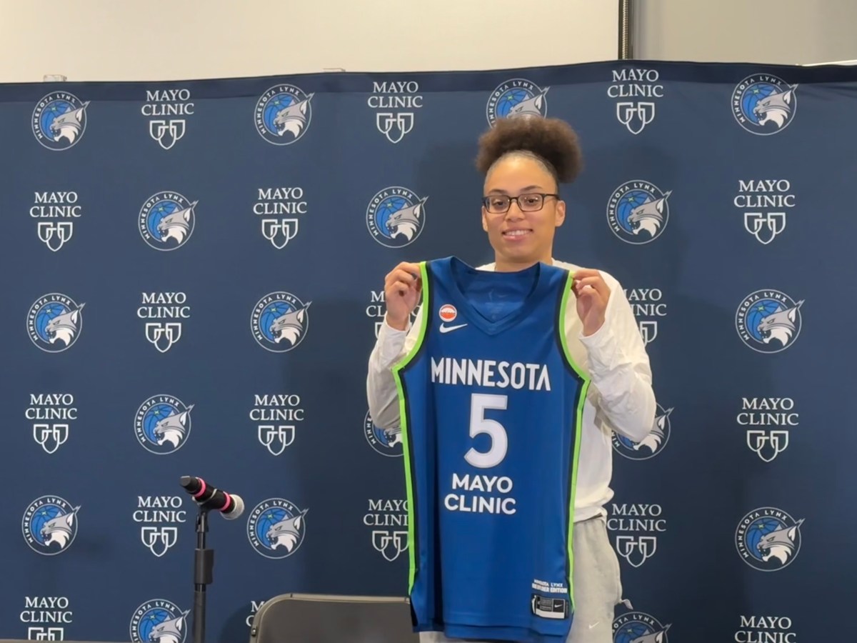 Olivia Miles holds up her blue jersey with 'Minnesota' written over the number 5.