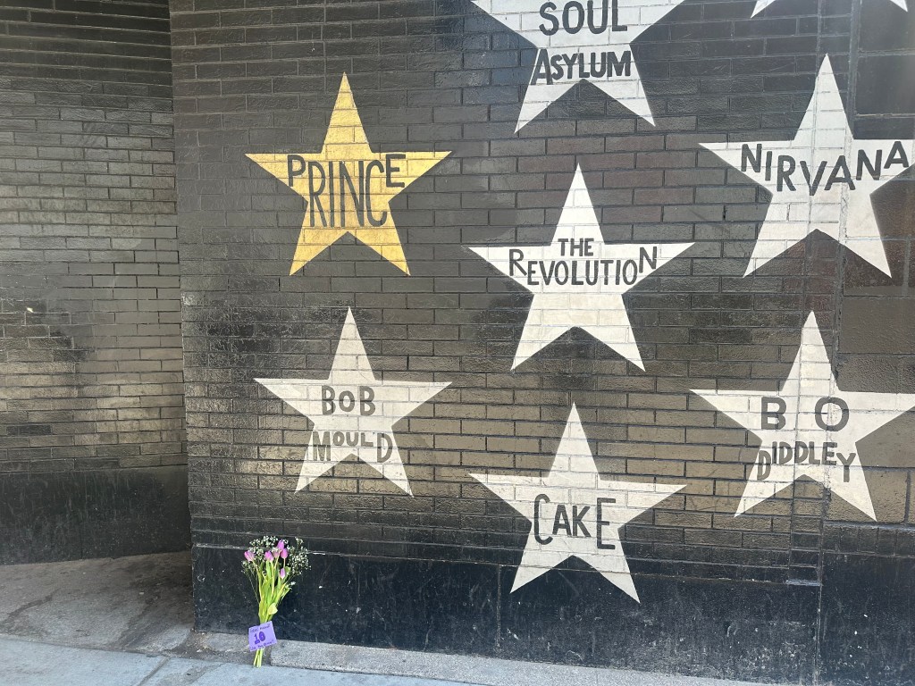 A black wall with several silver starts painted on it, one star that reads 'Prince' is painted gold.