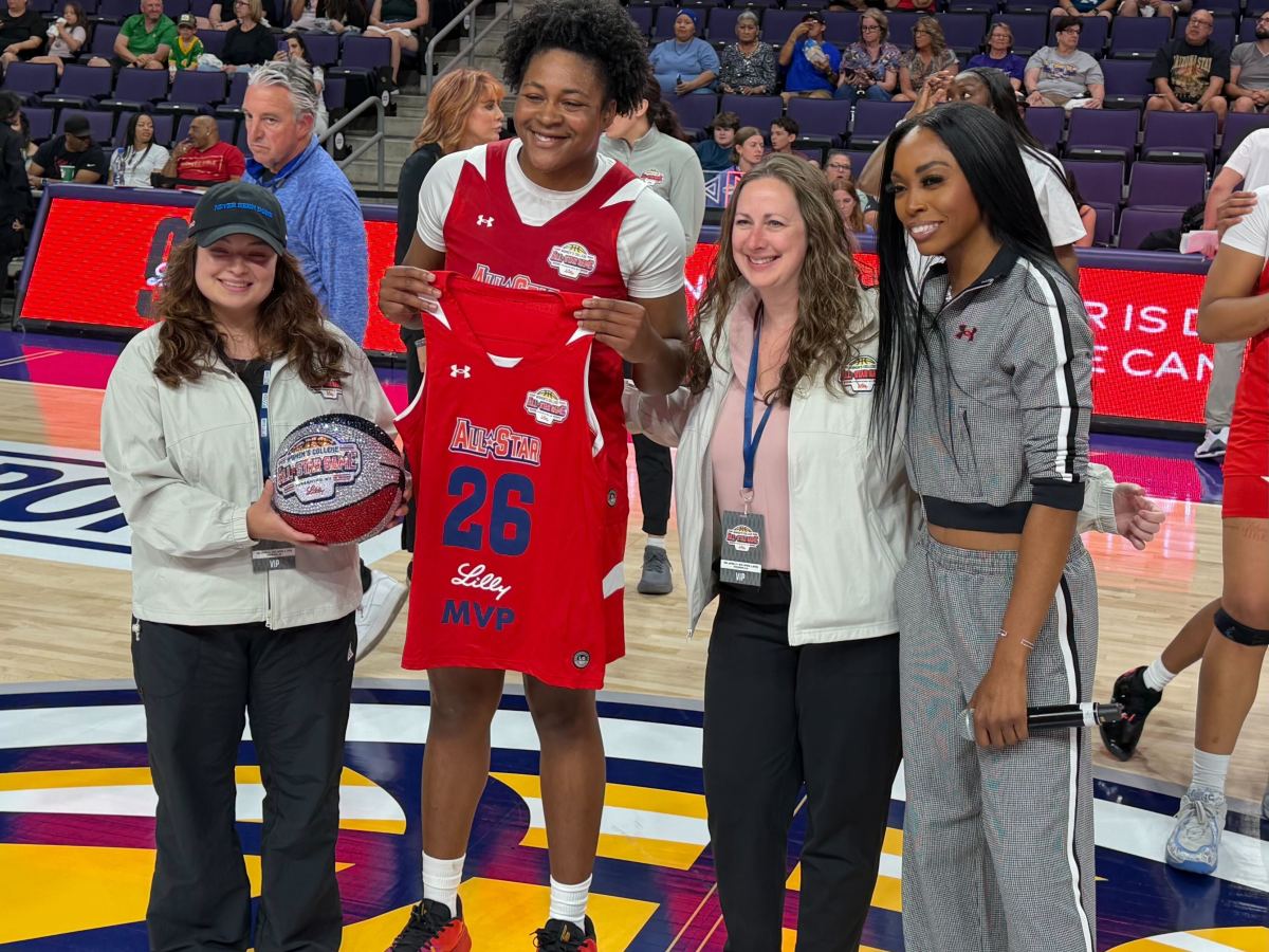 Christeen Iwuala smiling and holding an MVP jersey with a group on a court. A woman holds a basketball. Crowd and event atmosphere in the background.