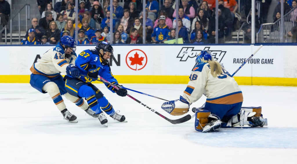 Two players battle for the puck in front while attempting a shot on net