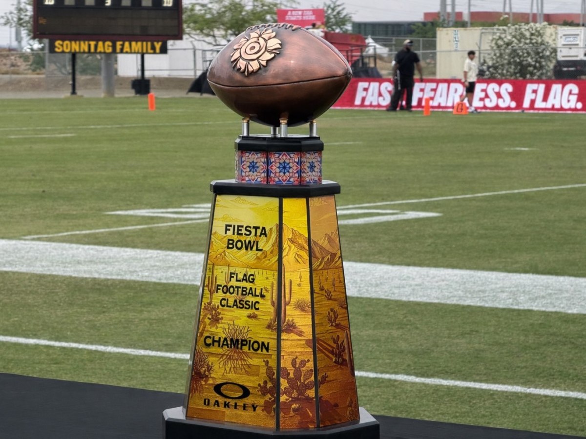 Trophy with a football on top and vibrant Southwestern designs stands on a football field. Text on the trophy reads "Fiesta Bowl Flag Football Classic Champion."