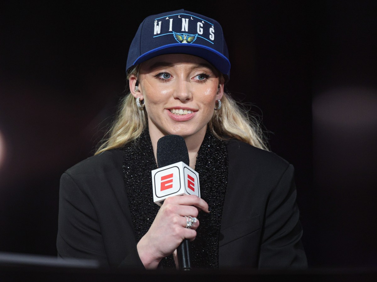 A basketball player with blonde hair wearing a blue cap speaks into a microphone