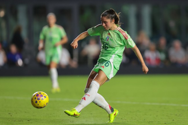 Giulia Dragoni, wearing a light green kit, kicks a yellow soccer ball.