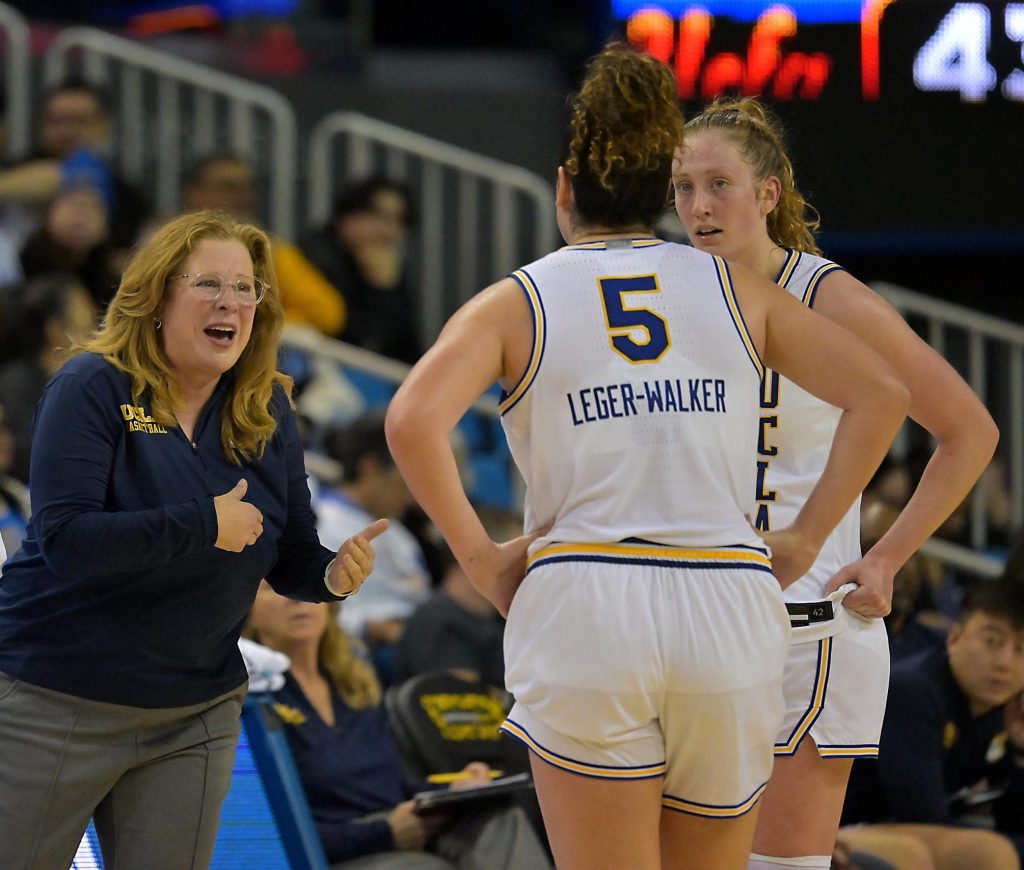 UCLA head coach Cori Close is wearing blue and using her hands to talk to her players who are wearing white uniforms.