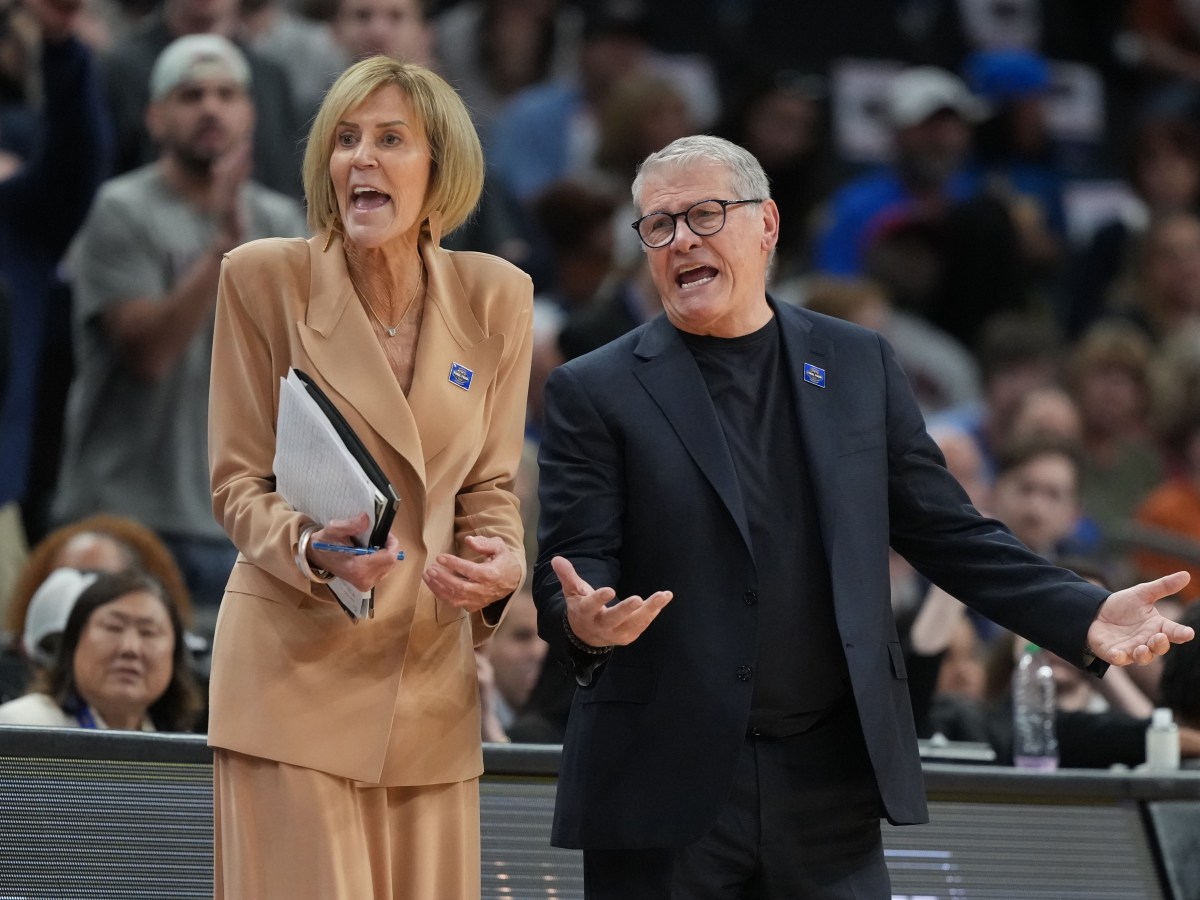 Chris Daily and Geno Auriemma react to action on the court with disbelief. Auriemma has his arms extended at about hip level and his palms turned up to the ceiling.
