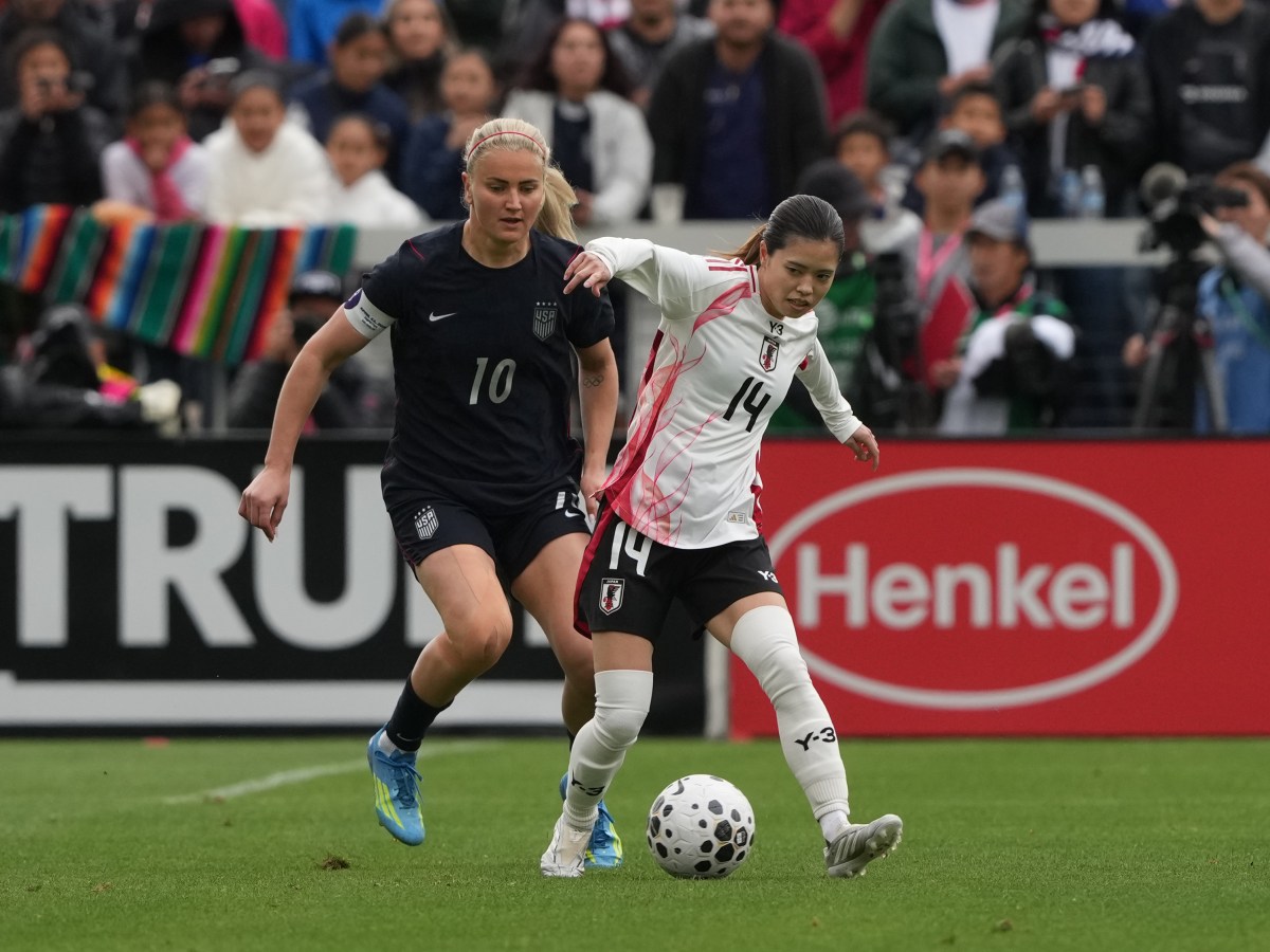 Two players battle for the ball, one in a black uniform and one in a white uniform, on a soccer field