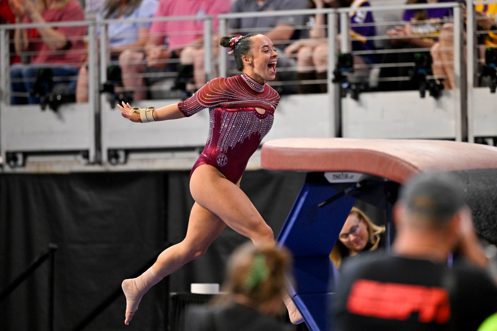 Faith Torrez celebrates her vault performance with her arms in the arm, wearing Oklahoma leotard