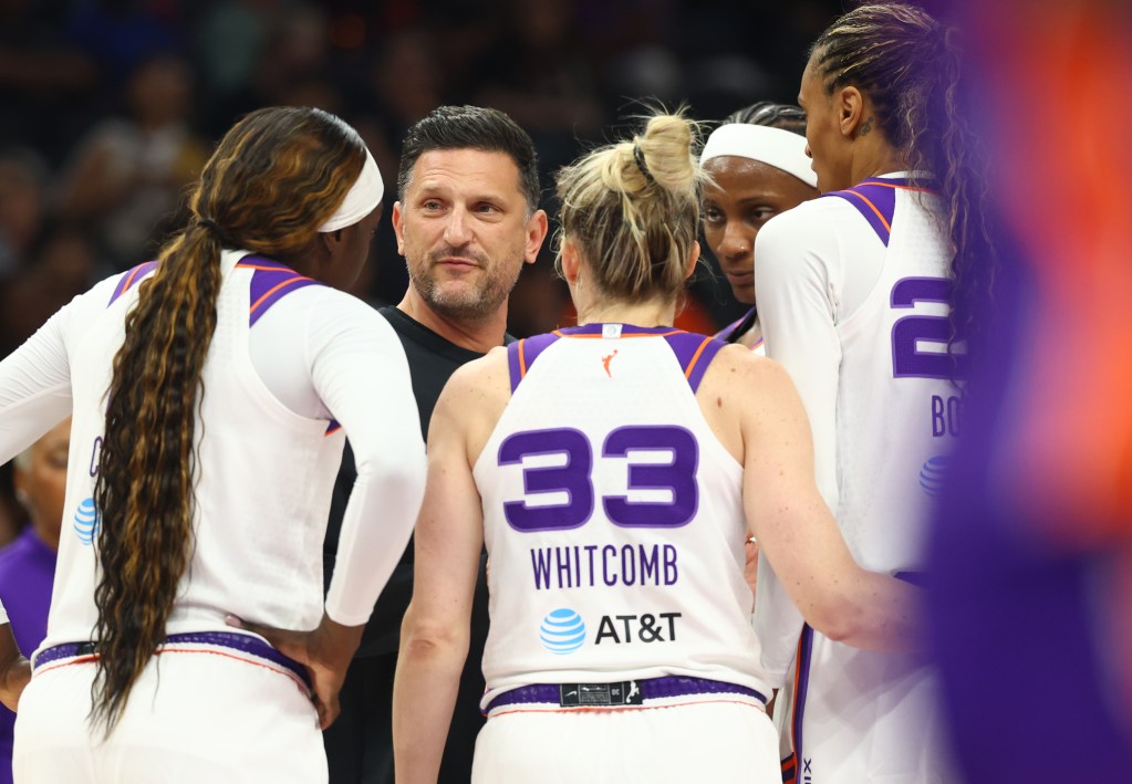 Nate Tibbetts giving instructions to a focused group of players in white jerseys with purple accents. The setting is intense and strategic.