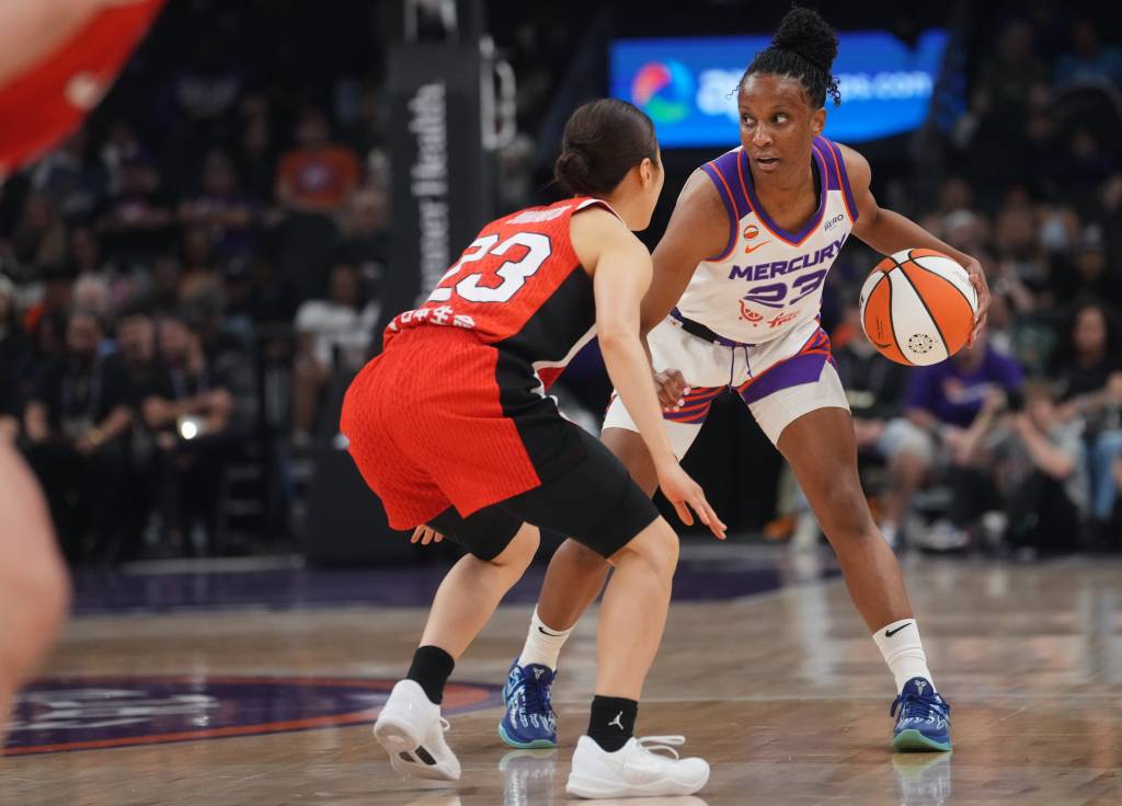 Kiana Williams wearing a white Mercury jersey dribbles, facing a defender in a red jersey. Both exhibit intense focus on a well-lit court.
