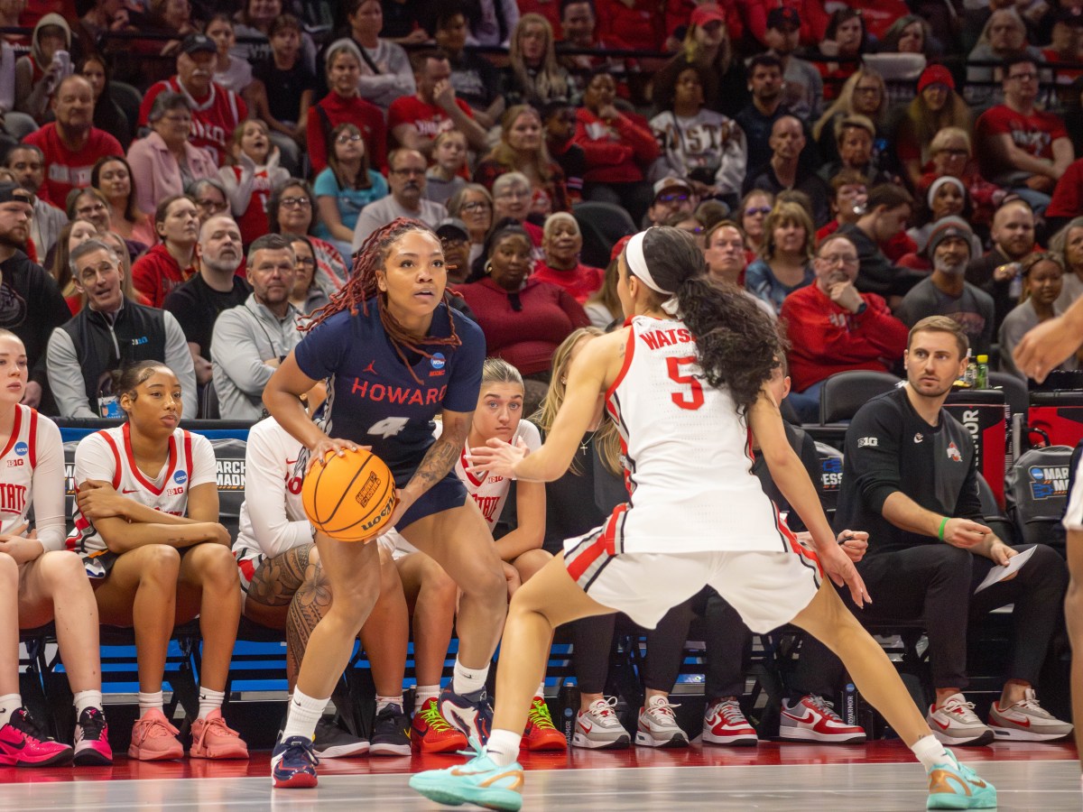 Howard's Ariella Henigan holds the ball at her hip with both hands as she looks up while being guarded by Ohio State's Ava Watson in front of the Ohio State bench.