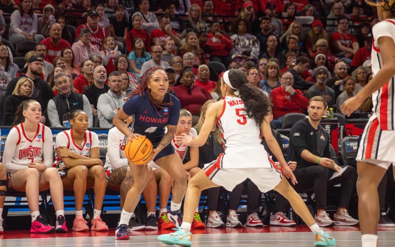 Howard's Ariella Henigan holds the ball at her hip with both hands as she looks up while being guarded by Ohio State's Ava Watson in front of the Ohio State bench.