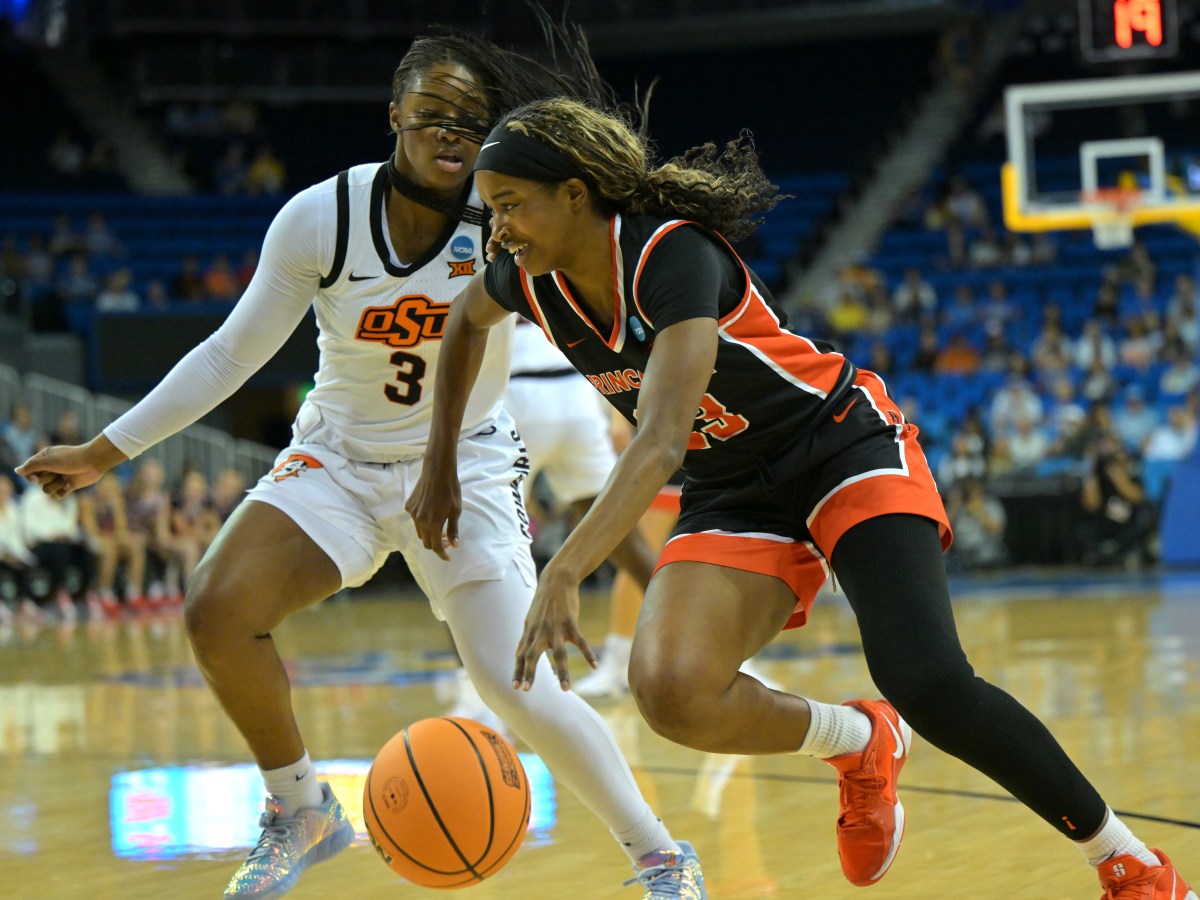Princeton guard Madison St. Rose dribbles with her left hand. She is shown moving from right to left, wearing a black jersey. An Oklahoma State defender is on her right hip, moving alongside her.