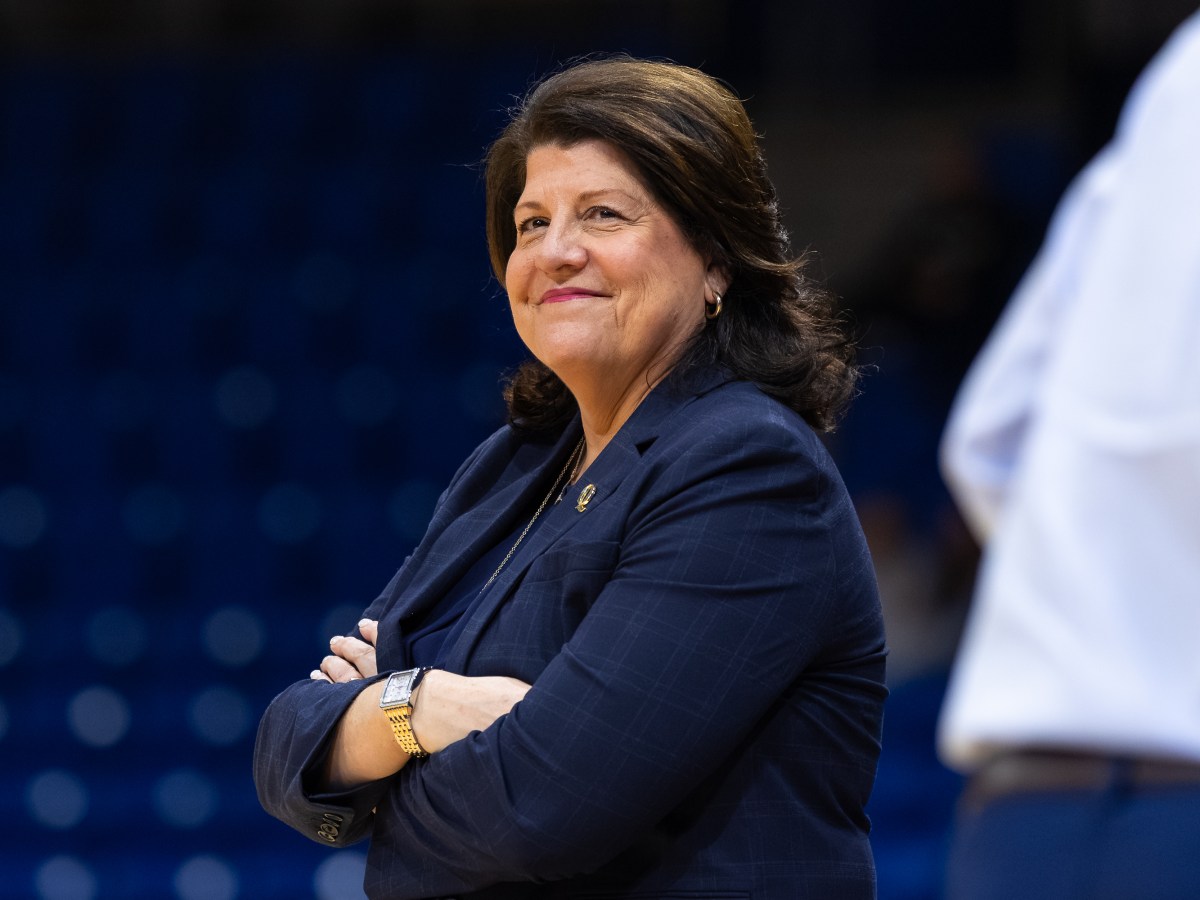 Quinnipiac head coach Tricia Fabbri stands with her arms crossed over her chest. Her head is turned roughly 45 degrees to the left, and she's smiling.