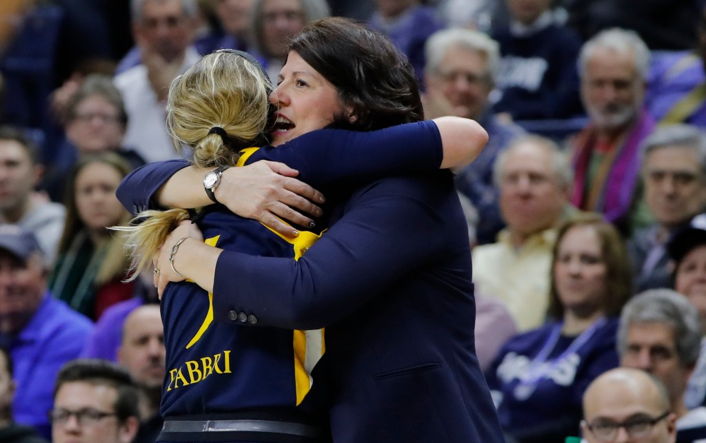 Quinnipiac head coach Tricia Fabbri tightly hugs her daughter, Carly, on the sidelines late in an NCAA Tournament loss. Carly is wearing her navy Quinnipiac jersey, and Tricia appears to be saying something in Carly's ear.