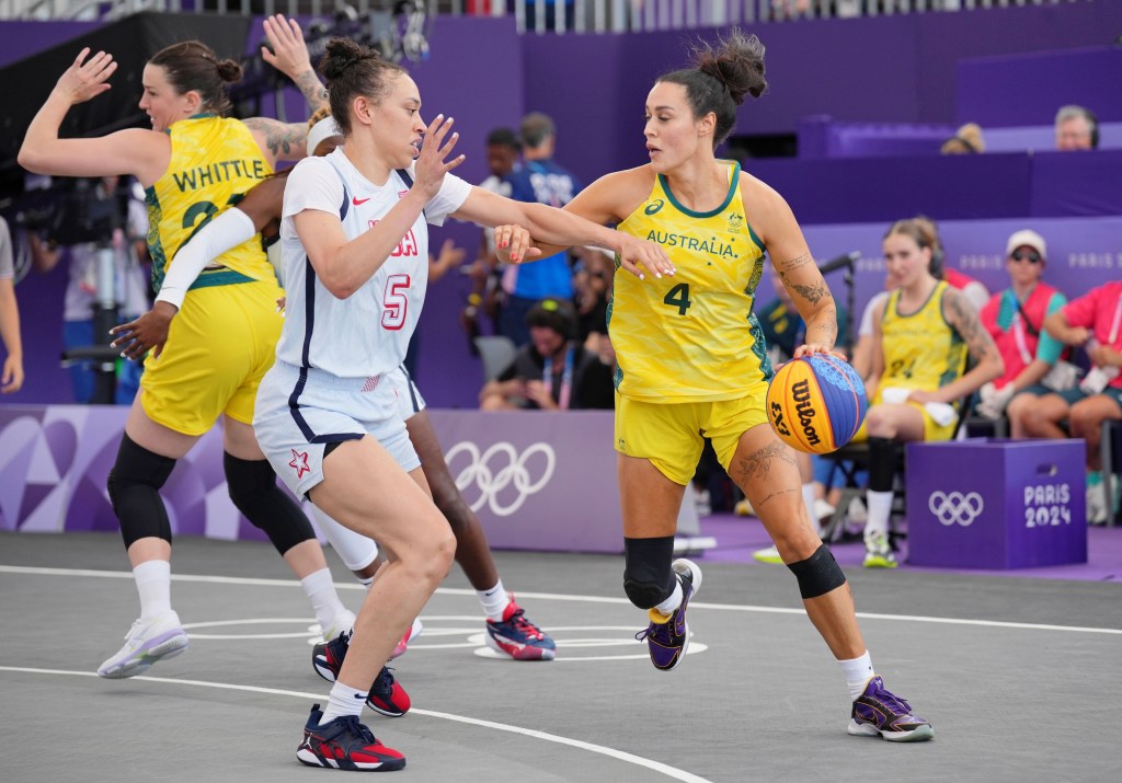 Australia guard Ally Wilson dribbles the ball with her left hand on the perimeter. United States forward Dearica Hamby reaches with her left arm toward the ball as she moves her feet laterally.