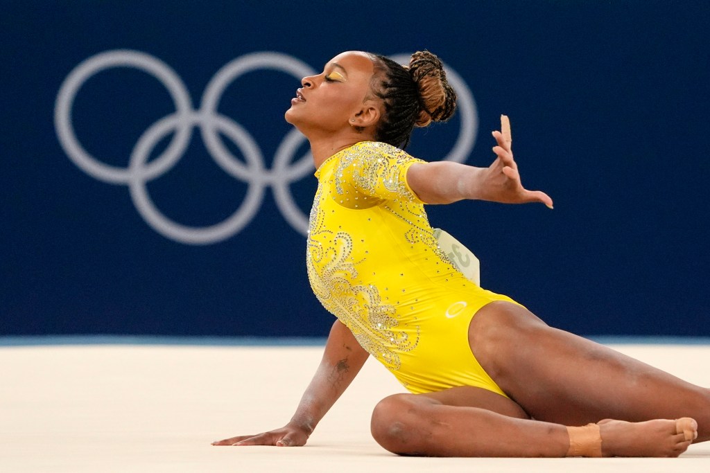 Rebeca Andrade wearing a gold leotard competes on the floor in front of the Olympic rings