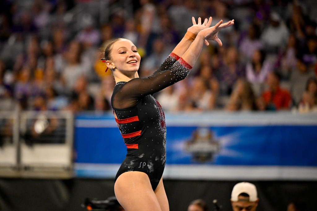 Gymnast Ana Borbosu performs in front of a crowd in a Stanford University leotard. She is smiling and her hands are raised.