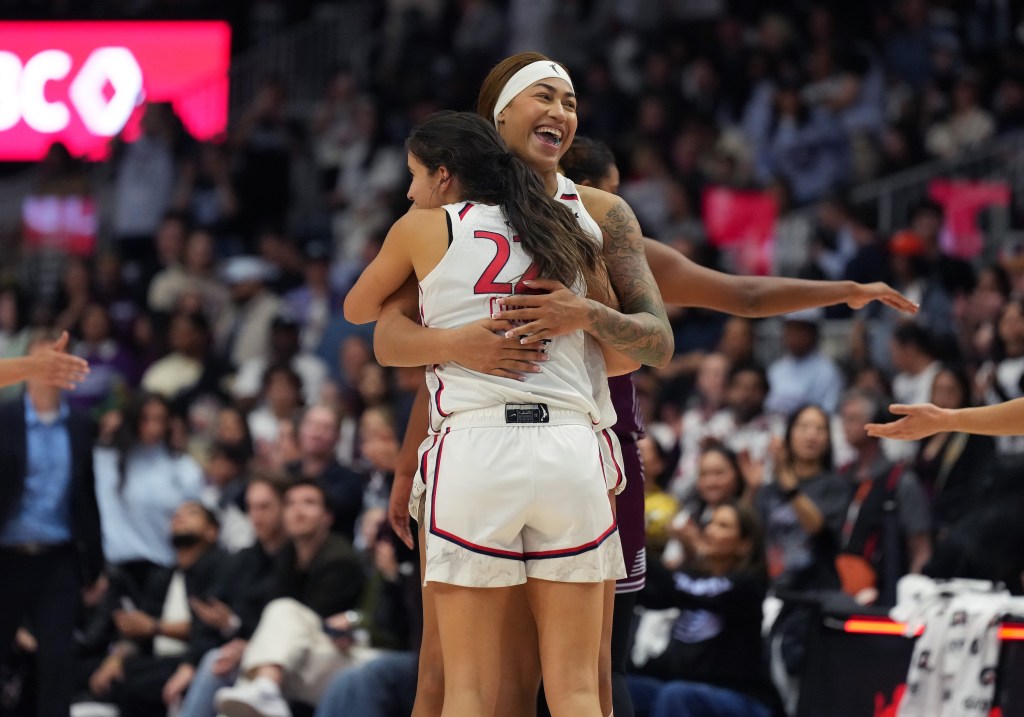 Washington Mystics center Shakira Austin hugs guard Sonia Citron and beams as they celebrate a season-opening win. Austin is facing the camera but looking off to her left, and Citron has her back to the camera.