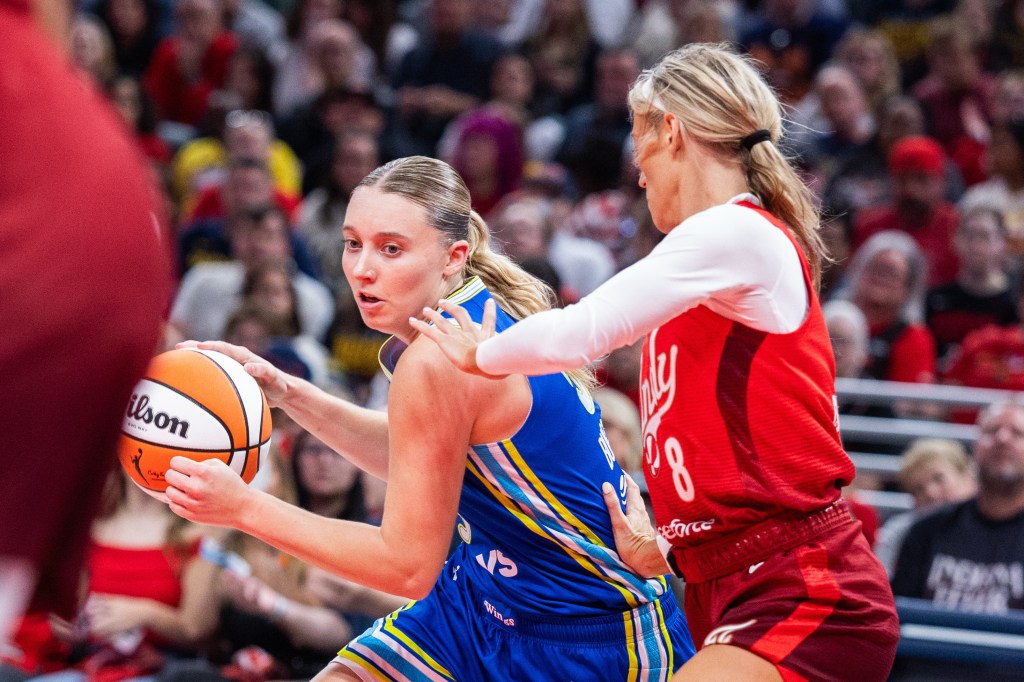 A player in a blue uniform and a player in a red uniform battle for the ball on a basketball court.