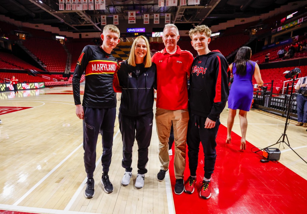 Four people stand together on a basketball court with banners hanging in the rafters.