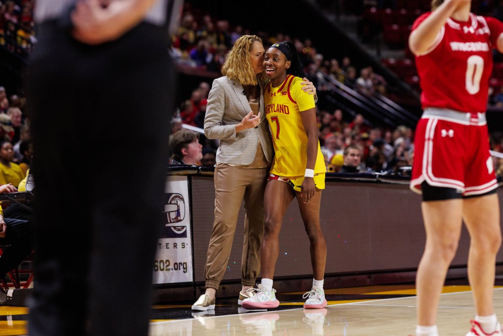 A Maryland player in a gold uniform laughs as head coach Brenda Frese whispers something into her ear.