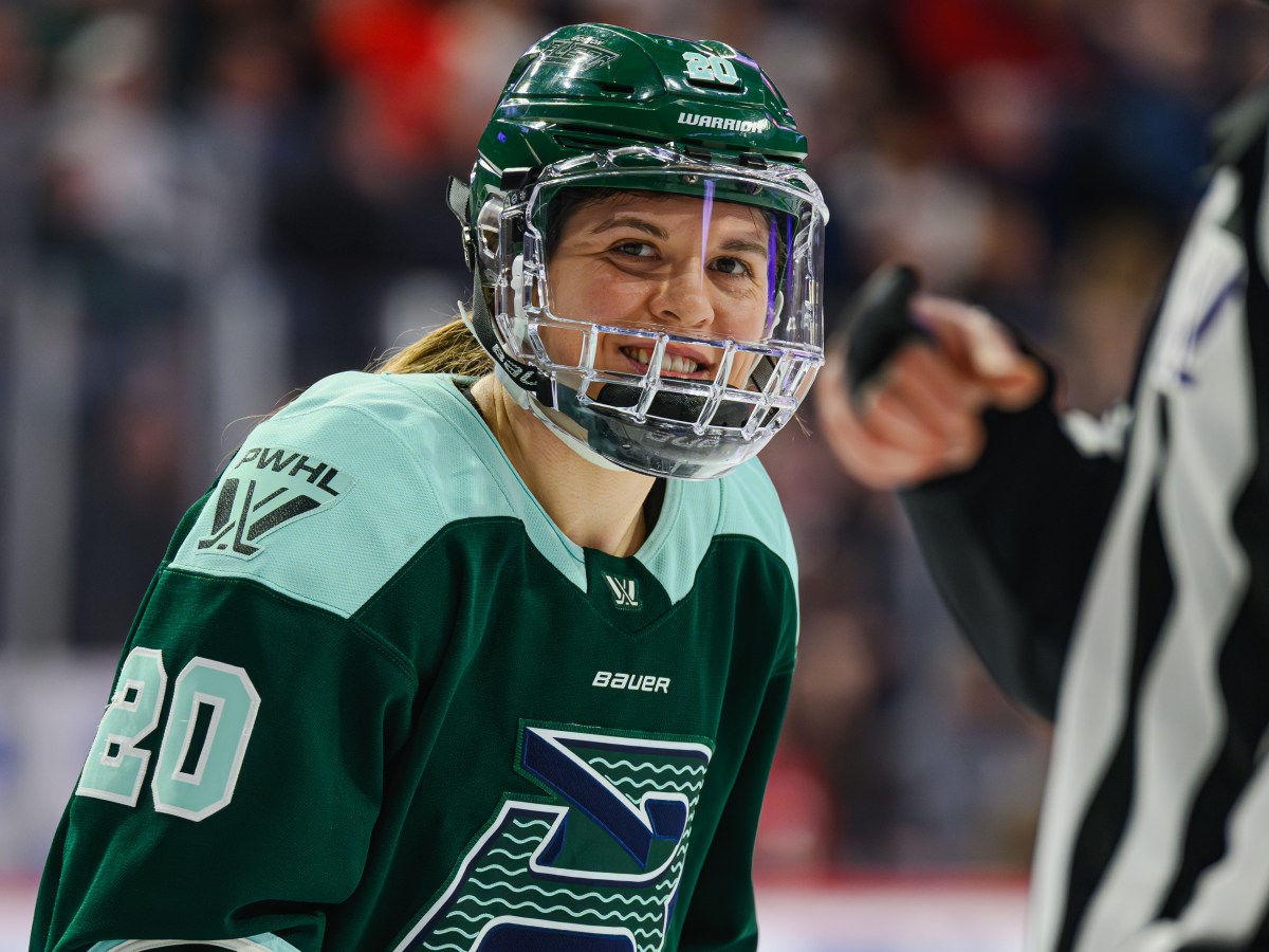 Brandt smiles as she prepares for a faceoff. She is wearing a green home uniform.