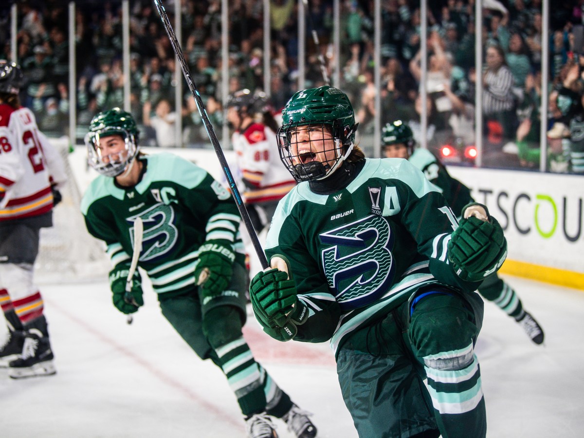 Müller yells and pumps her fists in celebration, as her teammates skate up to her to celebrate. They are all wearing green home uniforms.