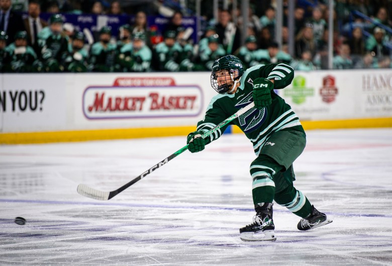 Winn leans forward and follows through with her stick as the puck sails toward the goal. She is wearing a green home uniform.