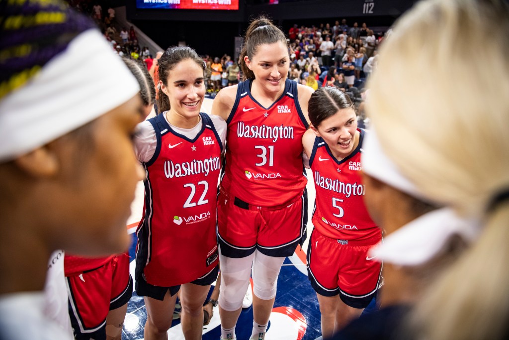 Sonia Citron, Stefanie Dolson and Jade Melbourne look towards a teammate with smiles on their faces in a whole team huddle after the game.