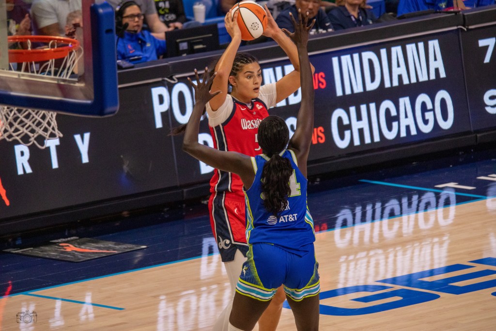 Washington Mystics center Lauren Betts holds the ball with two hands above her head. She is standing on the perimeter and looking for options.