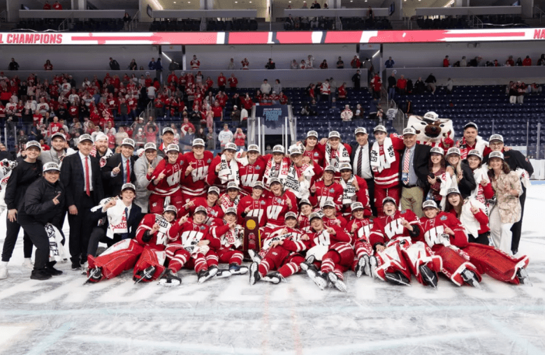 Wisconsin crowds around the 2026 national trophy at center ice in the Pegula Ice Arena