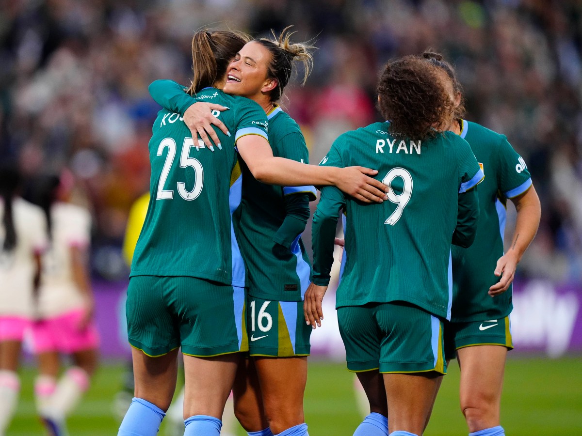 A group of players in green jerseys hug each other on a soccer field after a goal is scored
