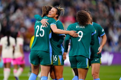 A group of players in green jerseys hug each other on a soccer field after a goal is scored