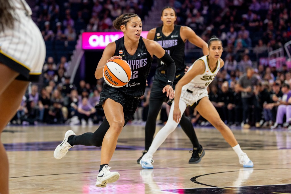 Golden State Valkyries guard Veronica Burton drives the ball. There is a Valkyries player and opposing player behind her. She is facing the camera with a large but out of focus crowd behind her.