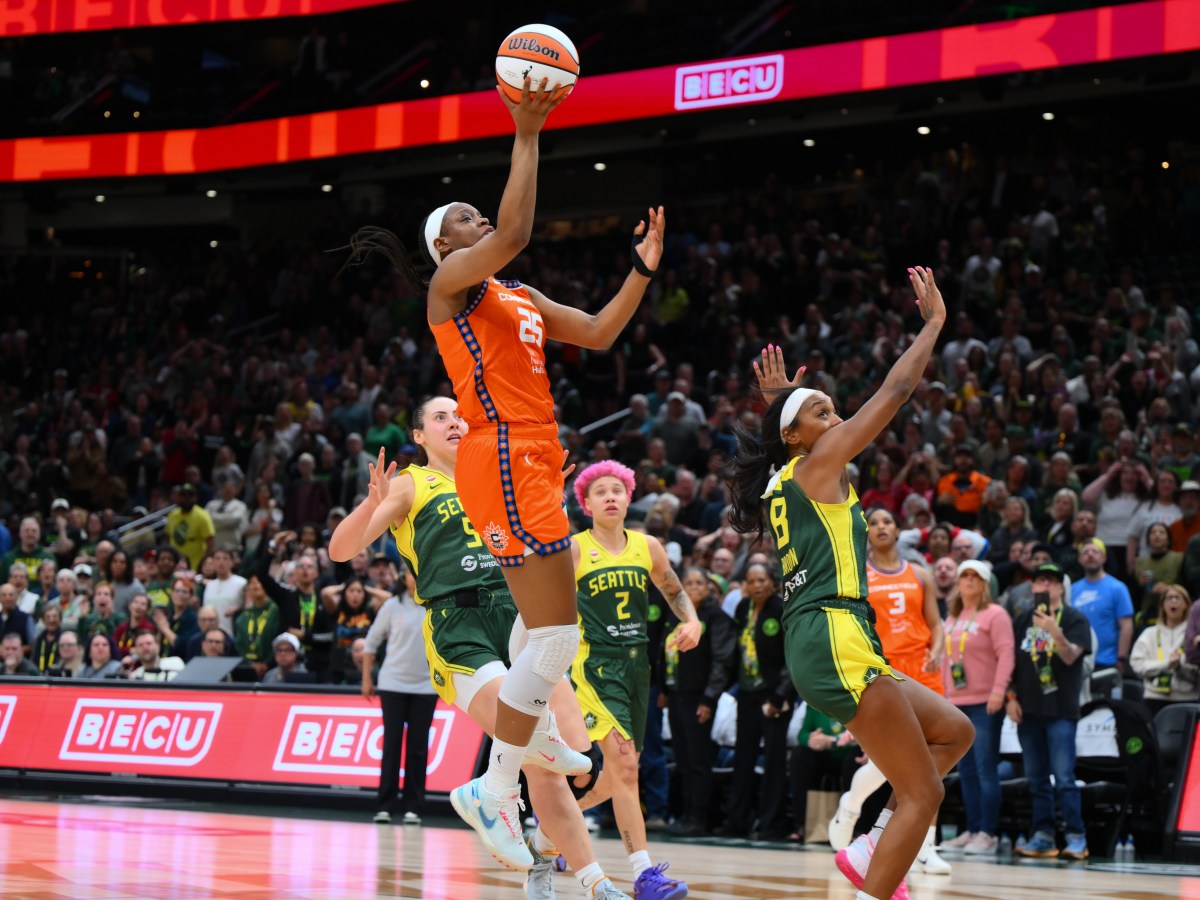 A player in an orange uniform jumps towards the basket and shoots the basketball