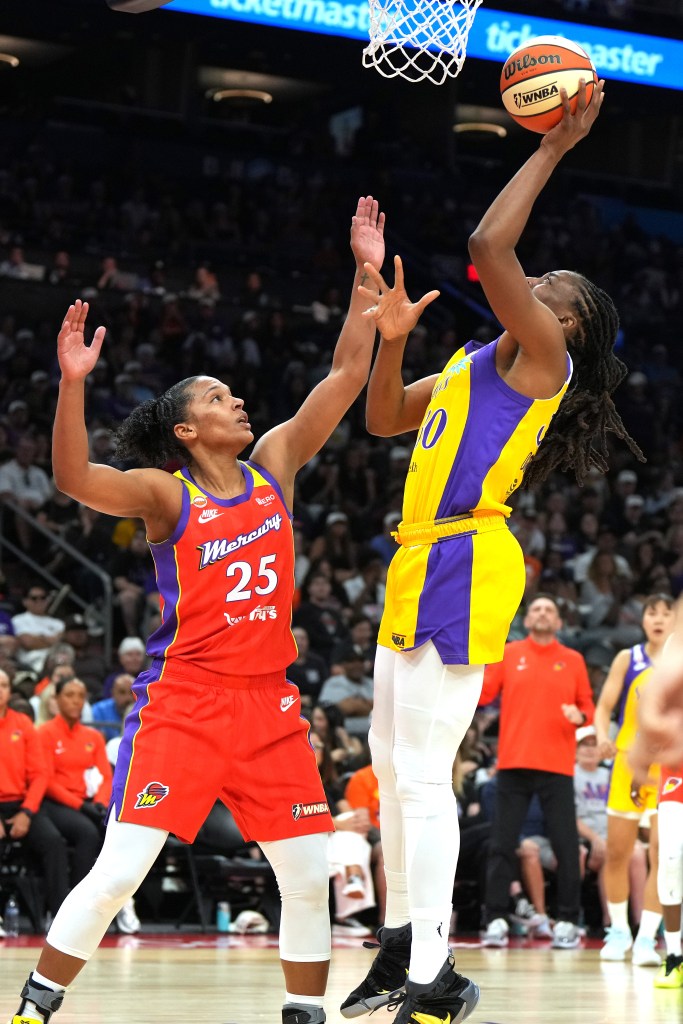 Los Angeles Sparks forward Nneka Ogwumike, wearing a yellow and purple uniform, shoots a left-handed layup at the rim. Phoenix Mercury forward Alyssa Thomas, wearing a red uniform, tries to contest it with her left hand.