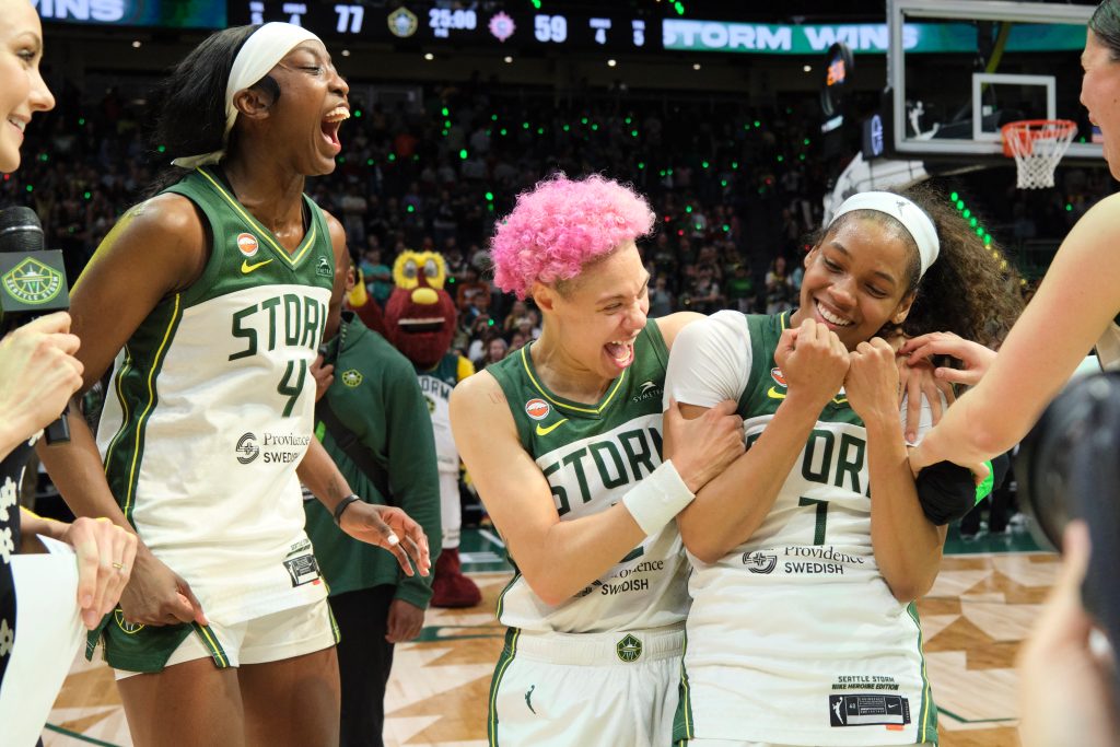 Flau'jae Johnson is on the far left, jumping up and down screaming in celebration while Natisha Hiedeman screams and hugs Zia Cooke's shoulders. Cooke shyly celebrates and holds her fists by her chin.