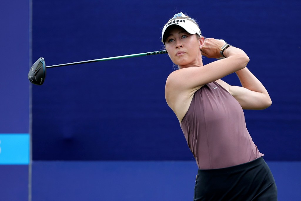Nelly Korda follows through on a tee shot and looks after her ball. Her hands are up by her hears in a follow-through position and the shaft of the club is parallel to the ground.