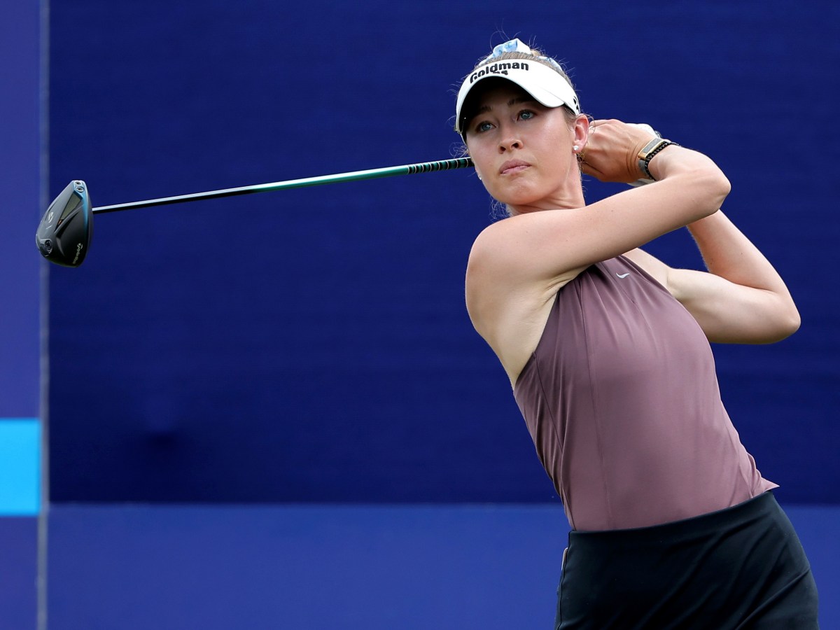 Nelly Korda follows through on a tee shot and looks after her ball. Her hands are up by her hears in a follow-through position and the shaft of the club is parallel to the ground.