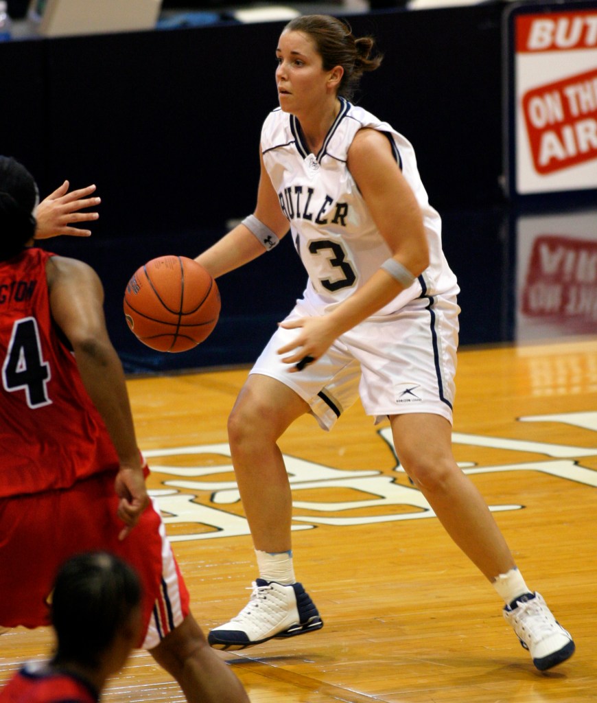Maria Marchesano, wearing a home white Butler jersey, handles the basketball during a college game photo from her time as a Butler student-athlete