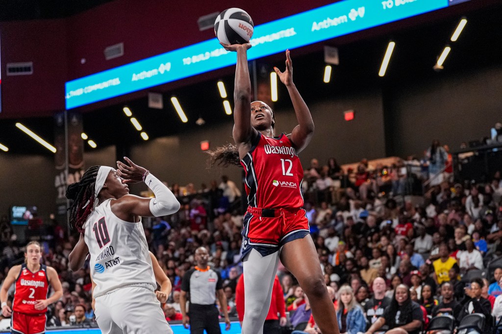 Washington Mystics wing Michaela Onyenwere shoots an open right-handed jump shot. Atlanta Dream guard Rhyne Howard pulls her hands back toward her head to avoid getting called for a foul.