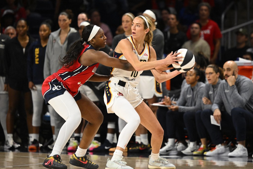 Indiana Fever guard Lexie Hull holds the ball with two hands away from her body as she scans the court. She's trying to protect it from Washington Mystics wing Michaela Onyenwere, who is reaching in to try to deflect it.