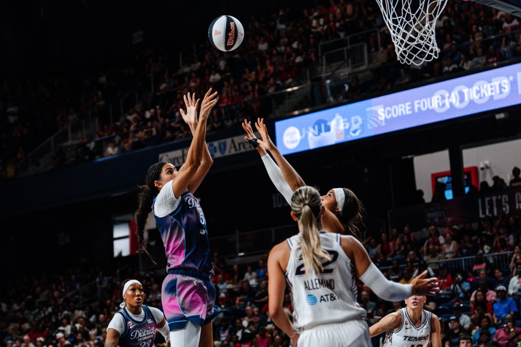 Washington Mystics center Lauren Betts rises straight up to shoot a short-range jumper over a Toronto Tempo defender. The ball has just left Betts' hands, and multiple players look on in the background.