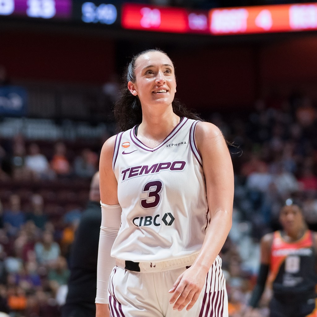 A basketball player in a purple and white Toronto Tempo jersey smiles on a basketball court