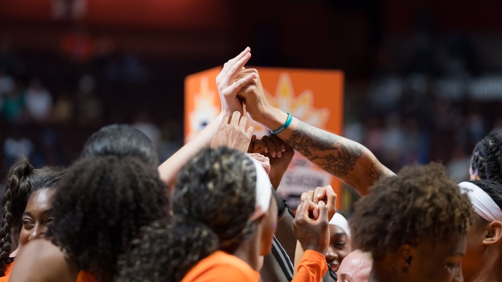 Connecticut Sun teammates huddle, holding their hands up in the middle. 