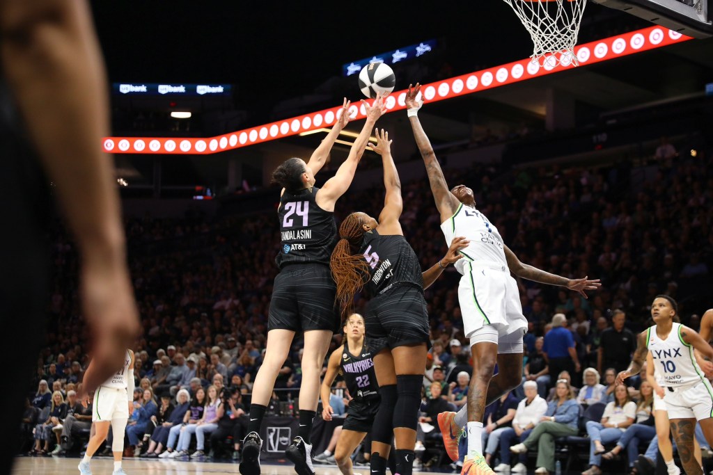 Golden State Valkyries forwards Kayla Thornton and Cecilia Zandalasini battle for a rebound against Minnesota Lynx forward Natasha Howard. Thornton and Zandalasini are shown from the back while Howard is shown from the front. Their are other players and a crowd behind them.