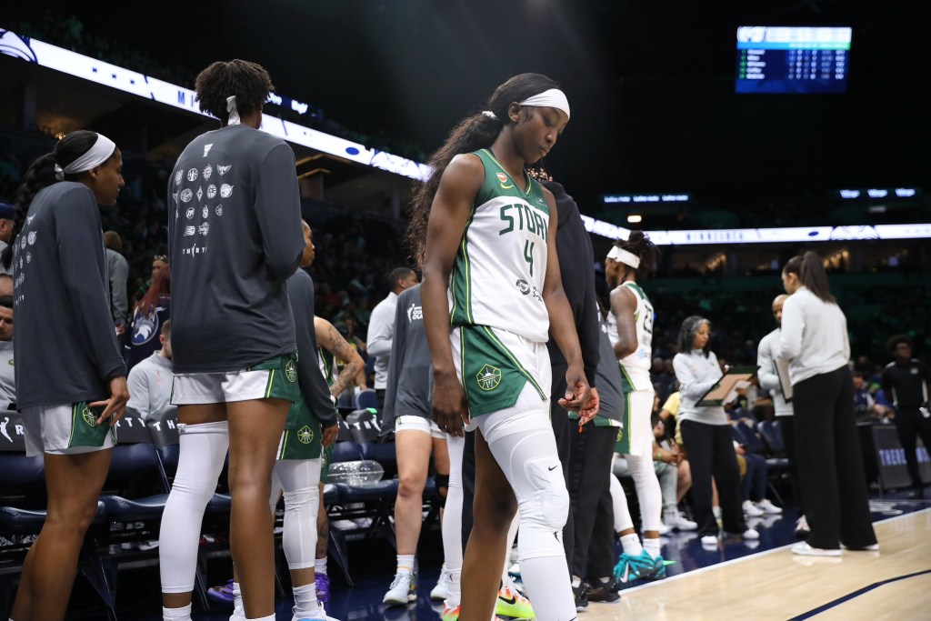 Seattle Storm guard Flau'jae Johnson walks away from a huddle where her teammates' backs are to her. She looks down towards the ground with focus and some somberness.