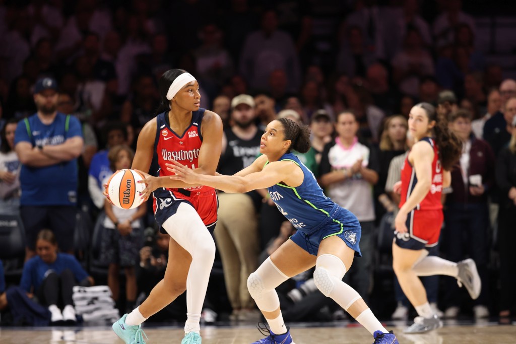 Washington Mystics forward Kiki Iriafen holds the ball with two hands near her right hip. A Minnesota Lynx defender is reaching to try to swat the ball away. Iriafen's head is up as she looks for options.